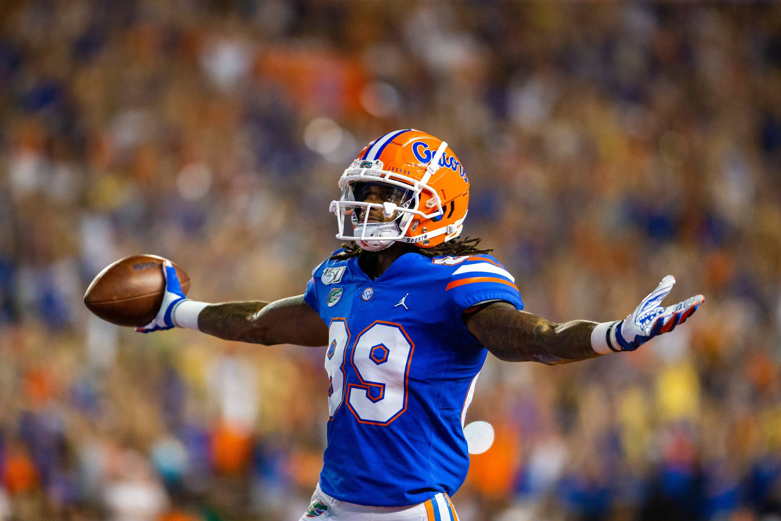 Football player holds his arms outstretched to the crowd with football in one hand after scoring a touchdown