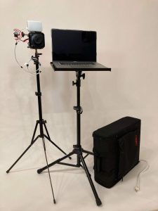 Camera setup on white background. A camera sits on a small stand next to a laptop on a similar size stand.