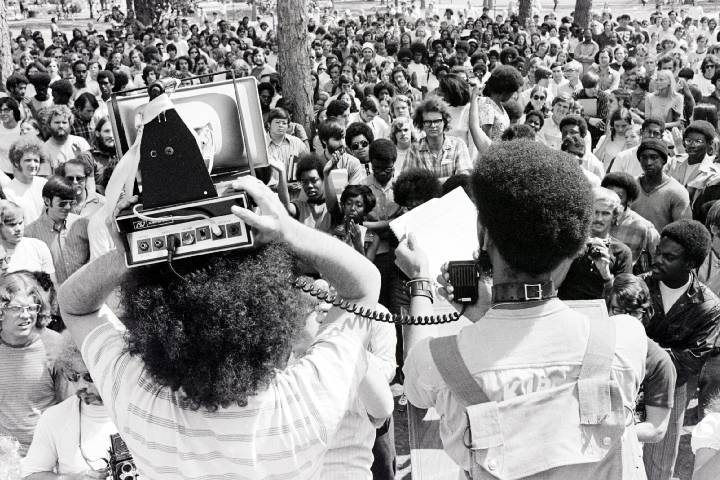 Two students, one with a loudspeaker above his head, address a large crowd.